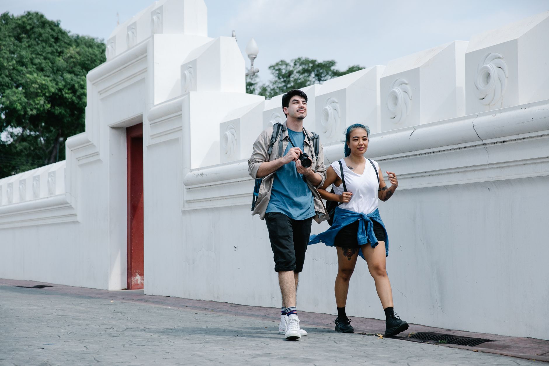 Young tourists exploring a city, walking by a historic white wall on a bright day. — Exploring Cuba's Cuisine: 5 Tips for Foo
