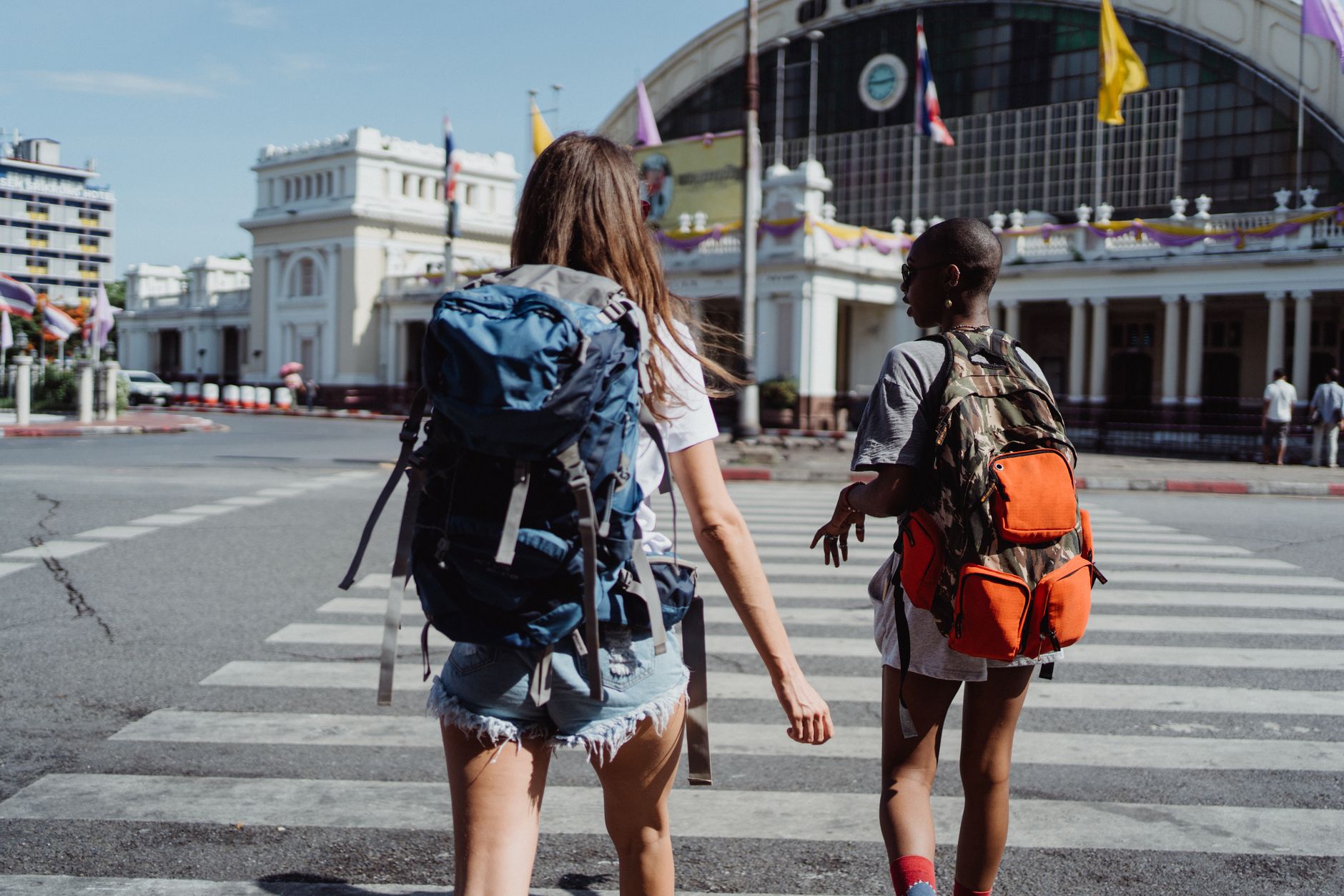 Two travelers with backpacks cross a city street near a historic building, symbolizing adventure and travel. — Exploring Lisb