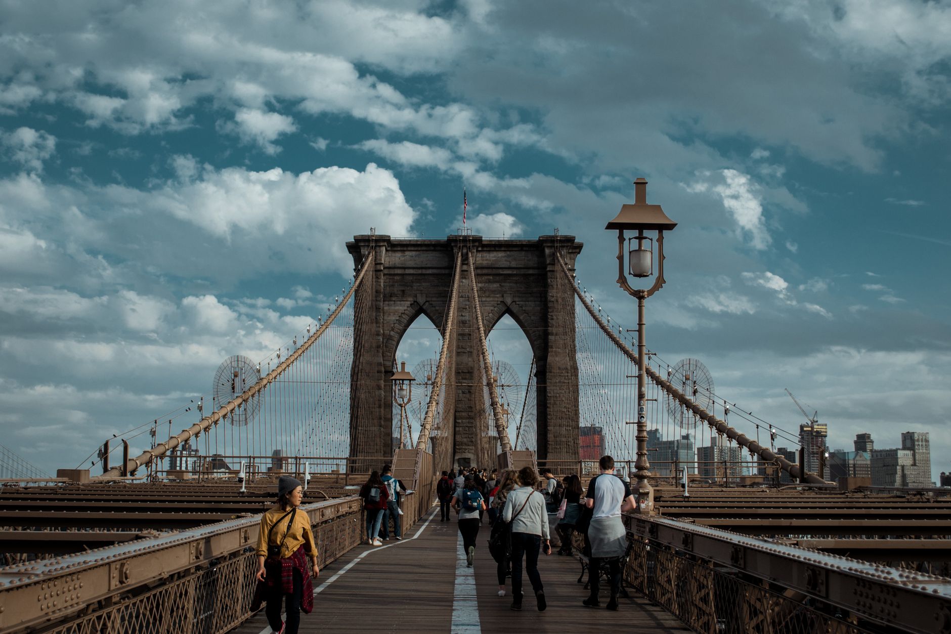 People walking on Brooklyn Bridge with a view of the Manhattan skyline under a cloudy sky. — Why TC Lottery Games Are Gaining