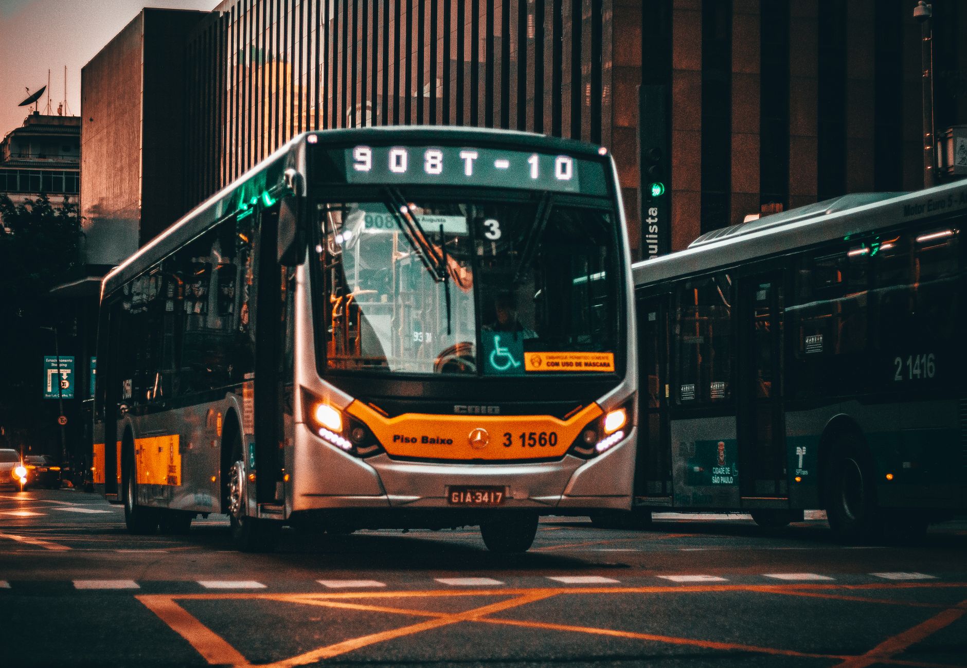 Low angle of modern bus riding on asphalt road amidst building of contemporary city at sunset — You Don't Have to Be a Trucke